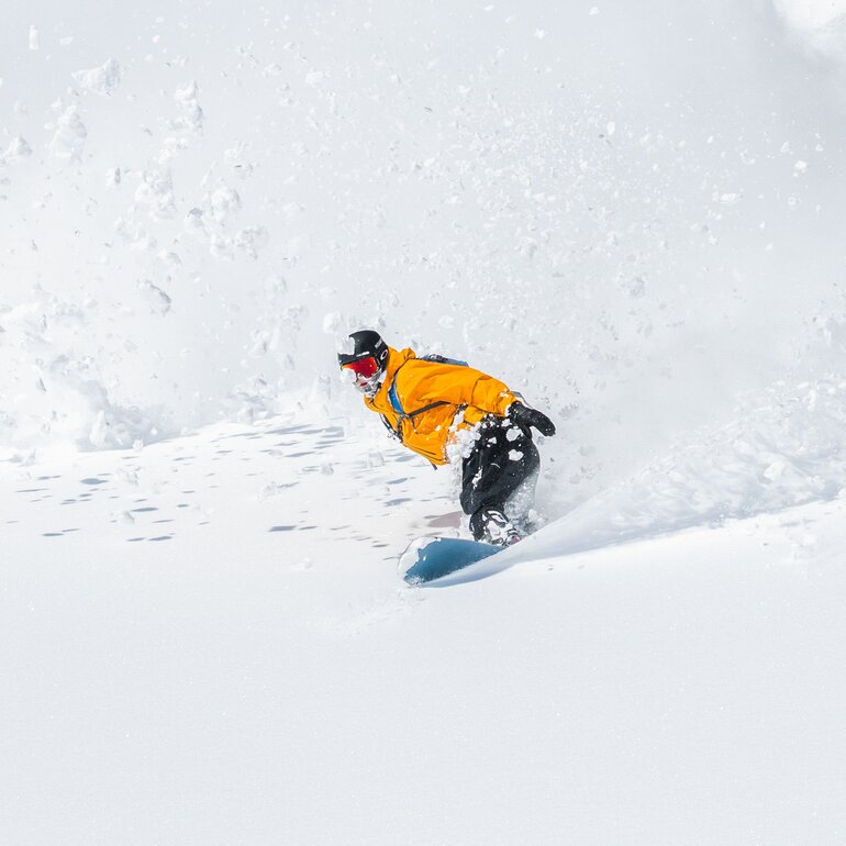 Snowboardfahrer gleitet fröhlich einen schneebedeckten Hang hinunter und hinterlässt frische Spuren im Schnee | © Laax